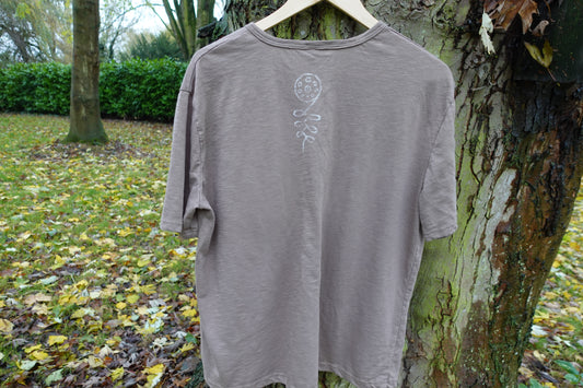 Back view of the taupe T-shirt outdoors, showing the hand-stamped design below the neckline