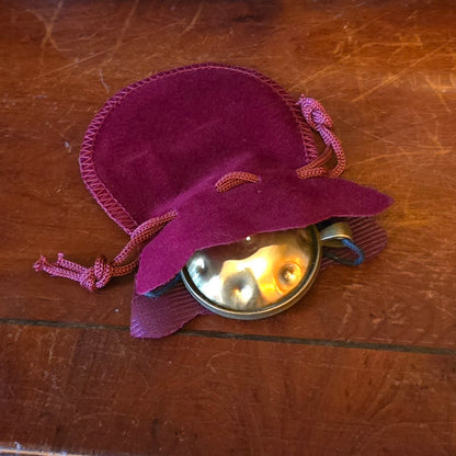 Brass Panshake pendant partially inside a soft drawstring pouch