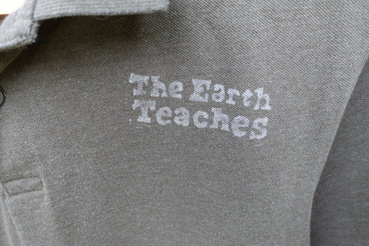Close-up of the ‘The Earth Teaches’ hand-stamped design on the green polo shirt