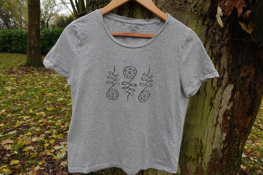 Light grey crew-neck T-shirt in UK size 10 hanging outdoors, showing the hand-stamped design on the front