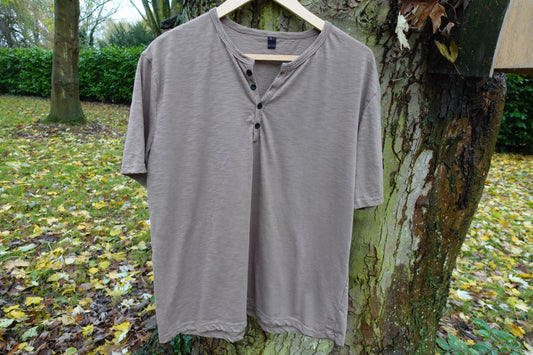 Front view of a muted taupe crew-neck T-shirt hanging outdoors, showing the plain front