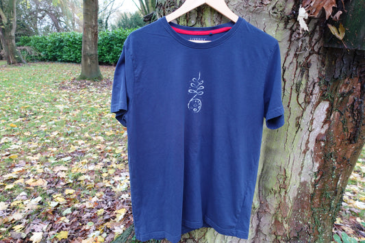 Navy blue crew-neck T-shirt hanging outdoors with a single vertical hand-stamped design on the chest.