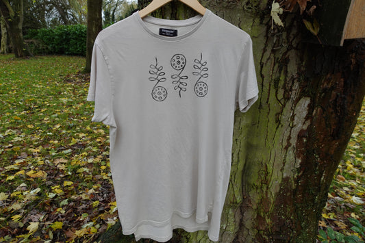 Light beige crew-neck T-shirt hanging outdoors, showing three hand-stamped designs across the chest