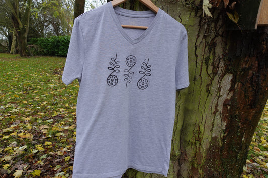 Light grey V-neck T-shirt hanging on a tree outdoors with three hand-stamped designs across the chest