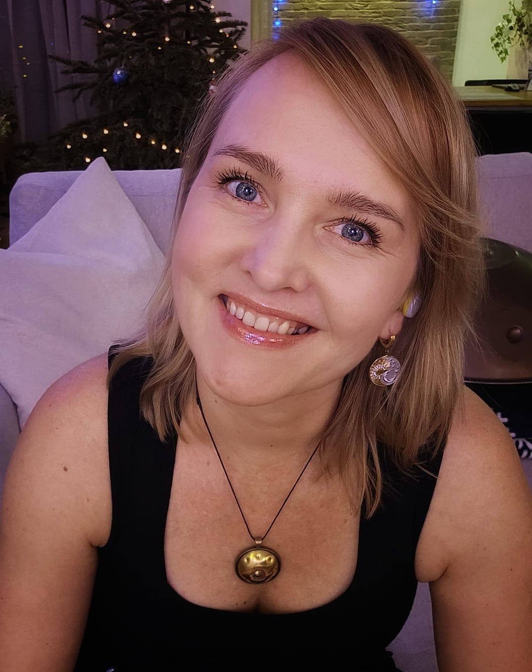 Woman with blonde hair and blue eyes smiling in a decorated room.
