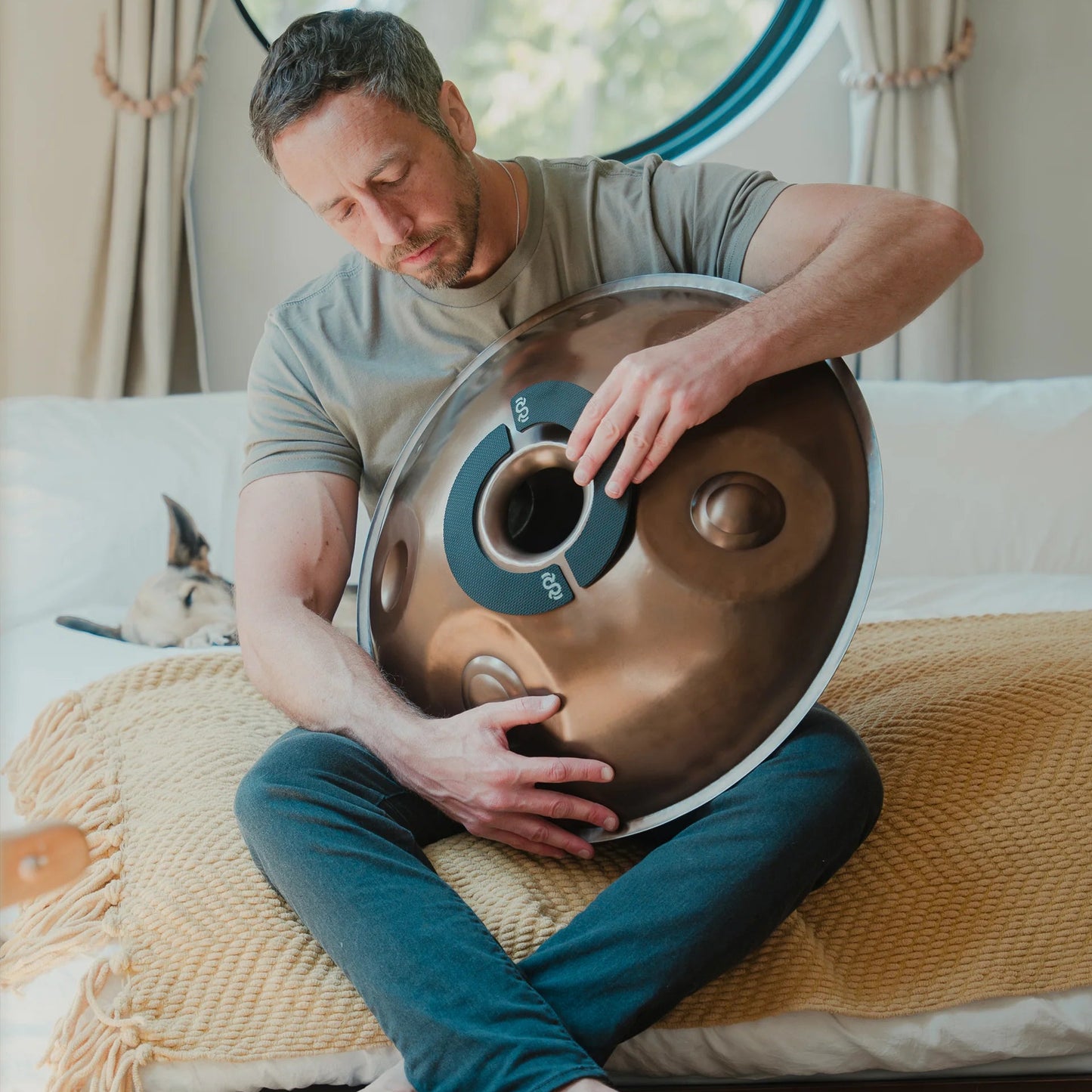 Person holding a handpan fitted with Rhythm Rest magnetic grips while seated indoors